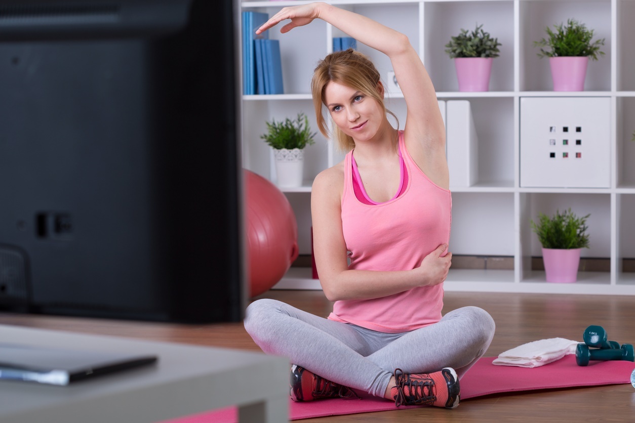 Mujer joven con ropa deportiva haciendo ejercicio frente a un televisor. Practicar deporte suave es beneficioso para aliviar el dolor de la fibromialgia reumática.
