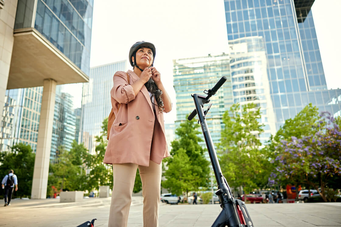 Mujer circulando en patinete eléctrico por un paseo urbano mientras lleva casco de protección